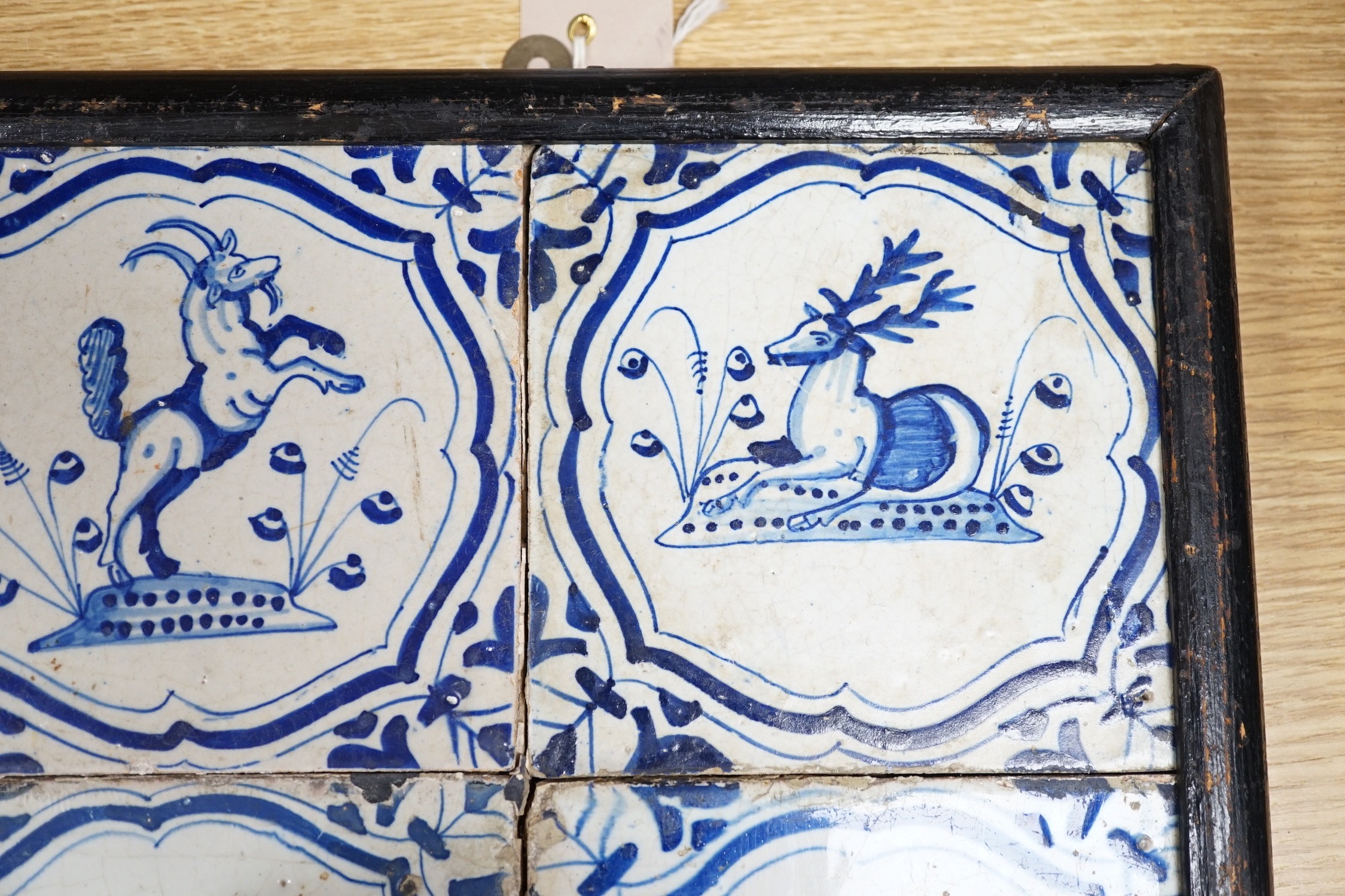 Four 17th century Dutch Delft blue and white tiles, decorated with deer, cockerels and figures within shaped panels (frame 29cm)